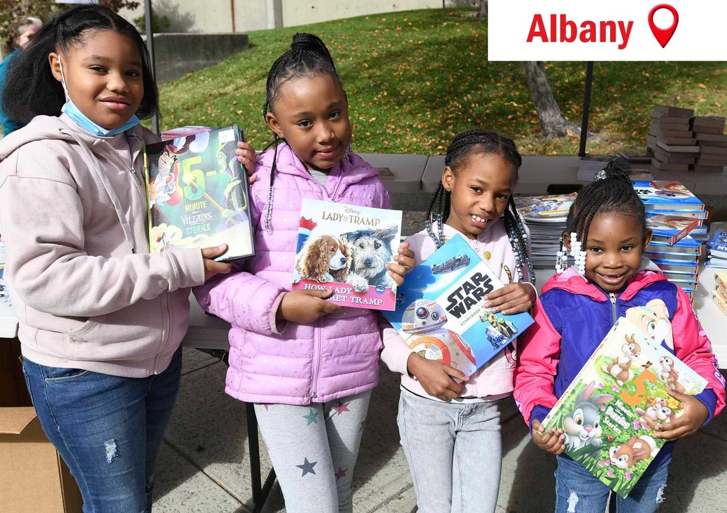 four young girls in Albany hold children's books at an event