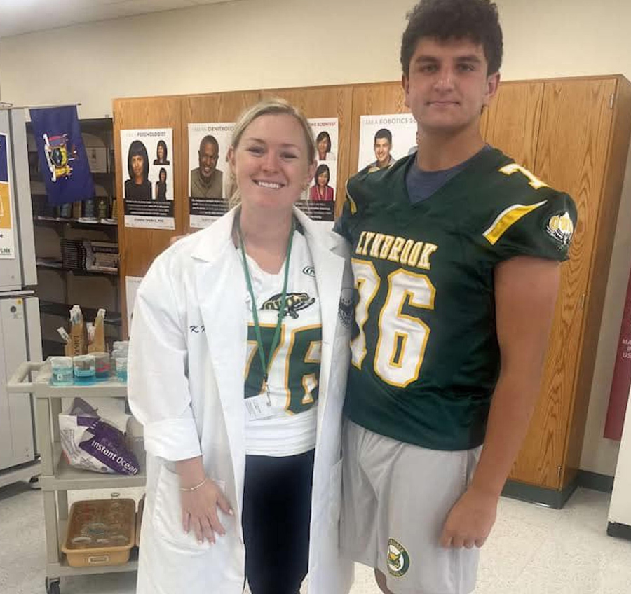 woman in jersey and lab coat smiling next to football player