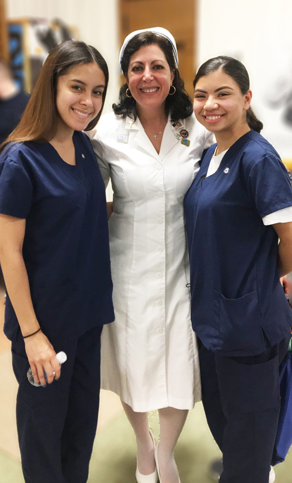 Linda Romano, center, pictured with two young women wearing dark blue scrubs