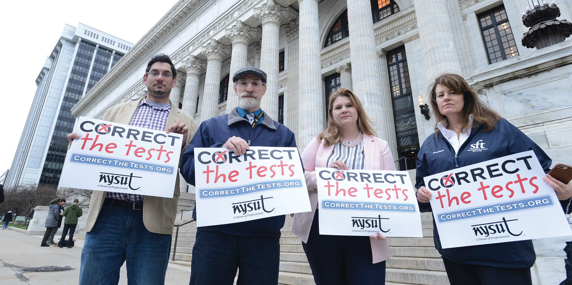 protestors holding signs that say "correct the tests"
