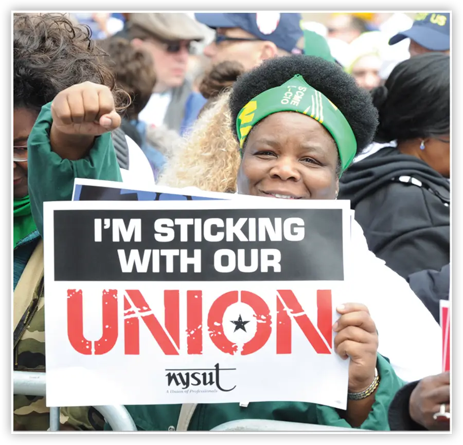 teacher holding up sign that reads IM STICKING WITH OUR UNION
