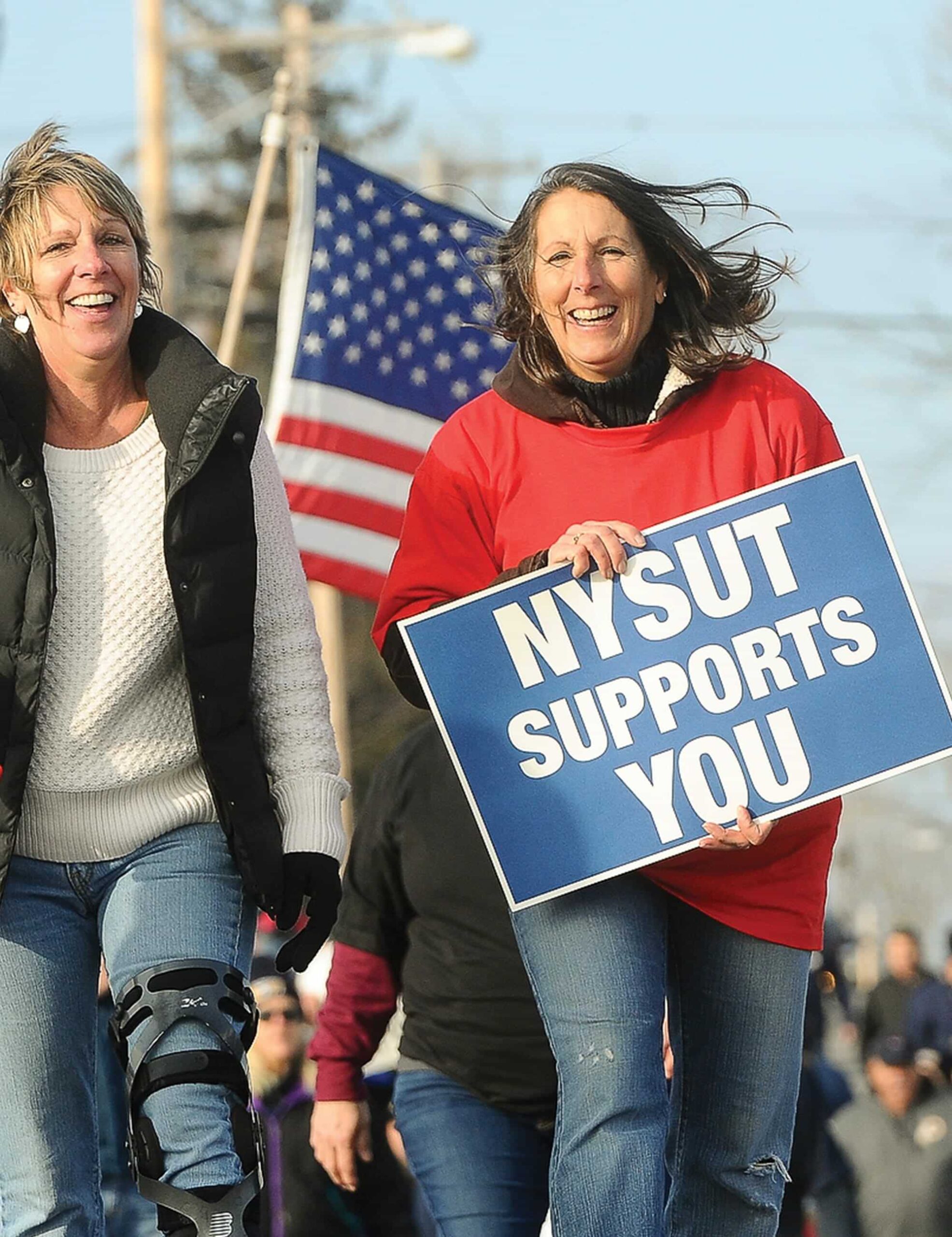two women smiling during protest while one holds a sign that says "NYSUT supports you"
