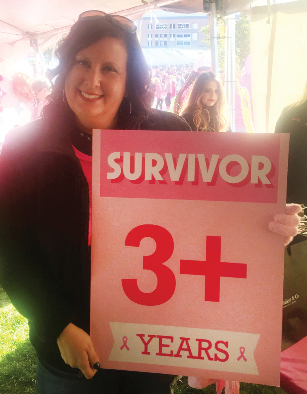 First-grade teacher Tara Pfohl holding a 3+ years survivor poster