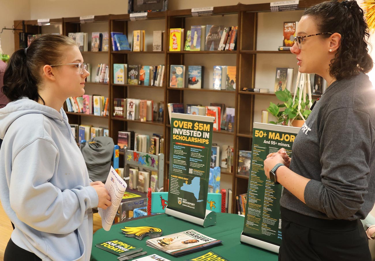 two young women talk while standing near a college promotion table in the Clyde-Savannah library
