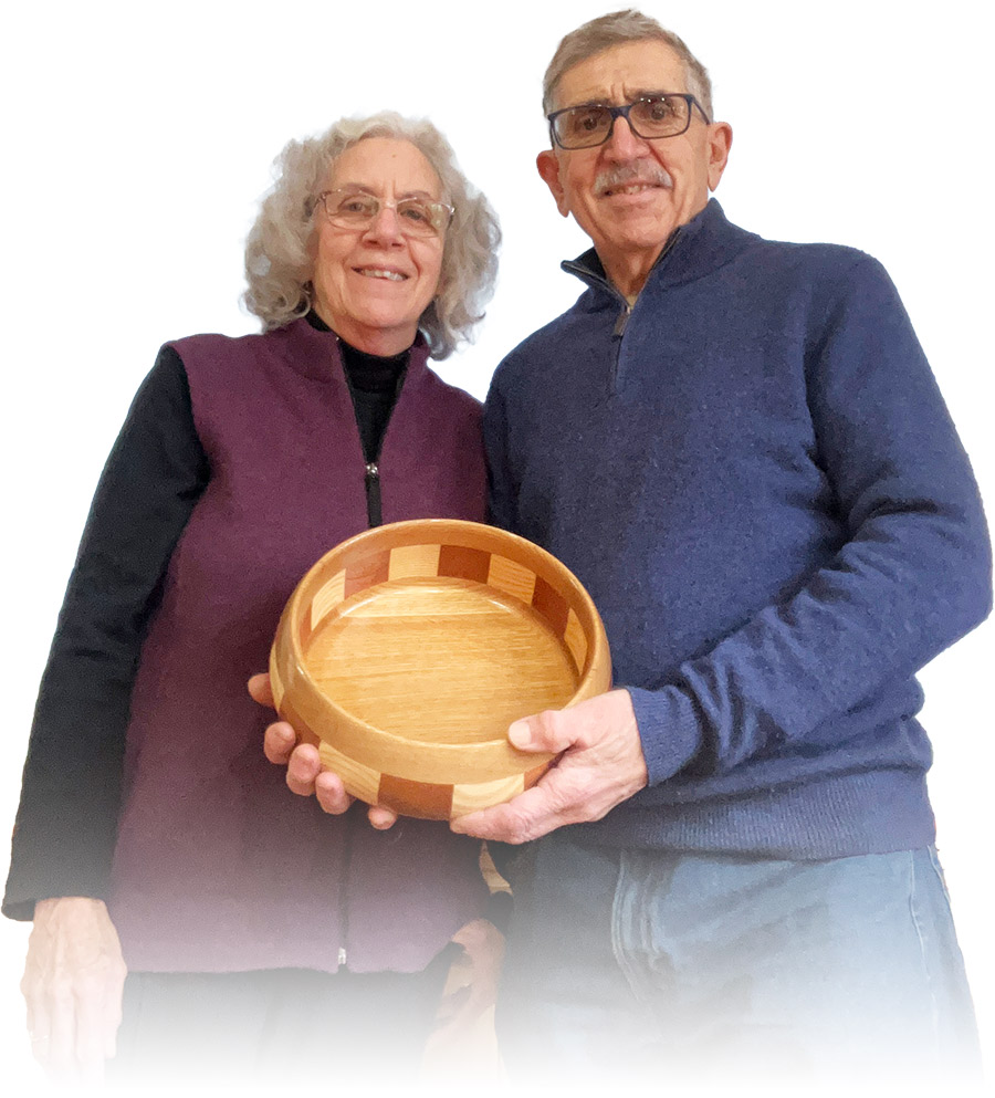 John and Jean Roccanova holding wooden bowl wearing fleece vests and sweaters