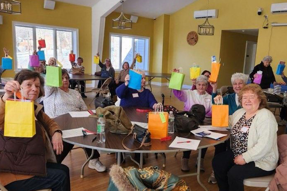 seniors sitting at tables in a community center hold up winter wellness packages in different colored bags