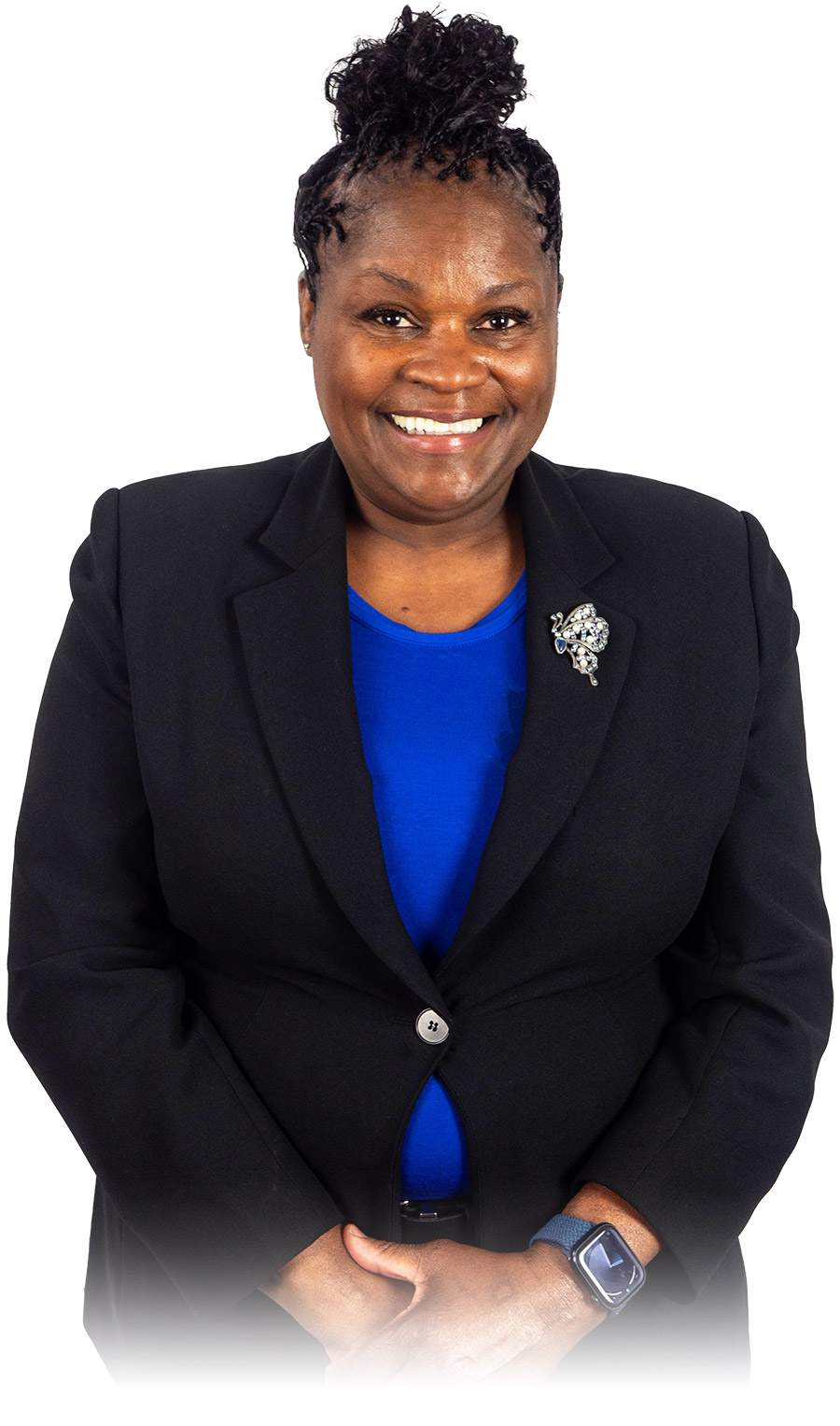 Portrait photograph close-up view of Kim Jones smiling and standing with her hands crossed over each other as she is wearing a black semi-closed buttoned business suit coat blazer, a blue dress shirt underneath, a smartwatch on her left wrist, and has a butterfly shaped decorative badge made up of jewels/diamonds pinned onto the business suit coat blazer within the heart area