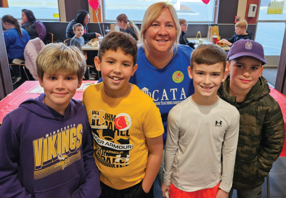 Kristen Roberg smiling with four male children in classroom