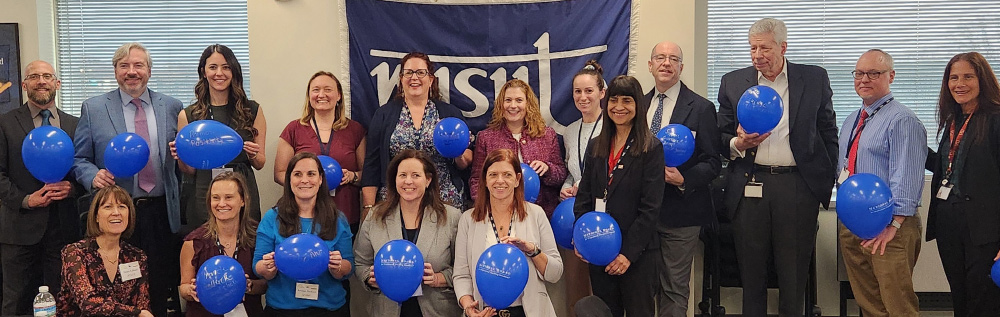 Long Island National Board Certified Teachers smiling side by side with blue balloons in hands in front of NYSUT banner