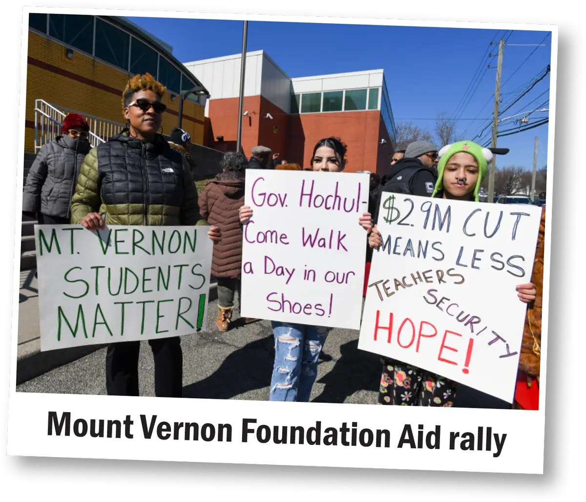 three attendees hold signs at the Mount Vernon Foundation Aid Rally