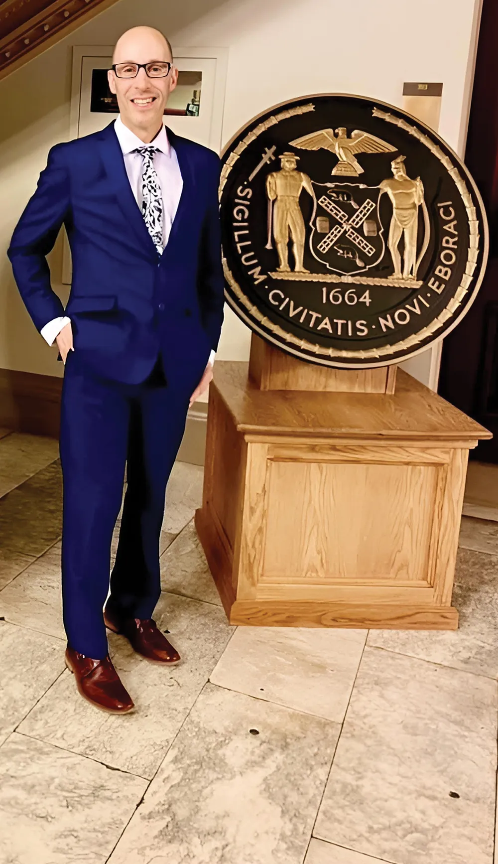 Jonathan Schulman in a suit and tie standing next to a large coin on display