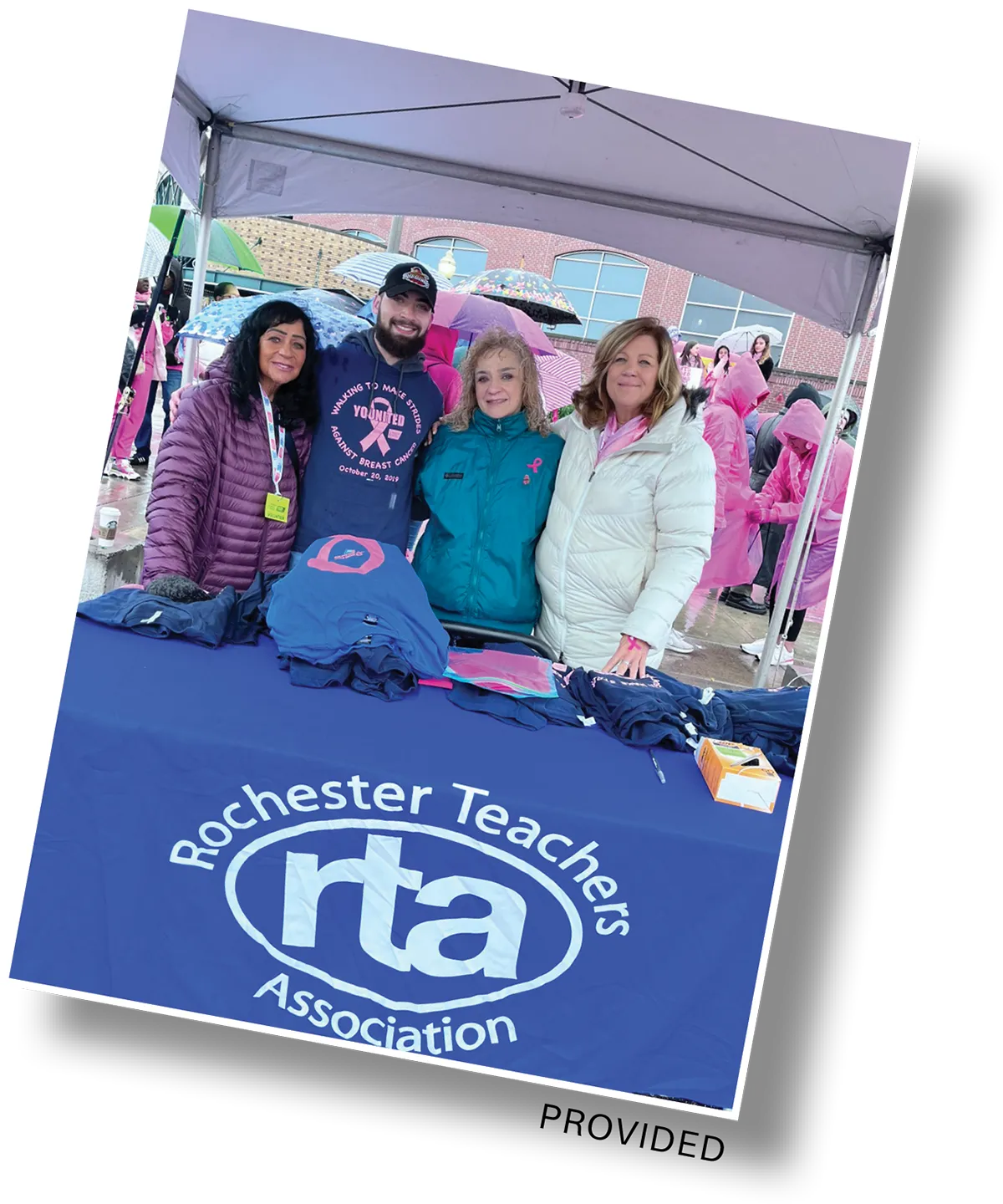 Group of four people at a table with the Rochester Teachers Association logo under a canopy.