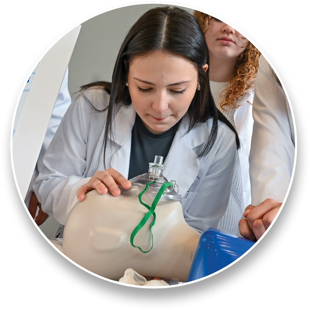A woman in a lab coat practices on a medical training mannequin with an oxygen mask.
