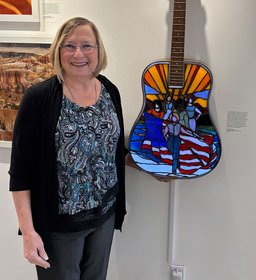 Kristine Huchthausen pictured beside her artwork titled “Wielding Our Collective Power”, made of an acoustic guitar and stained glass
