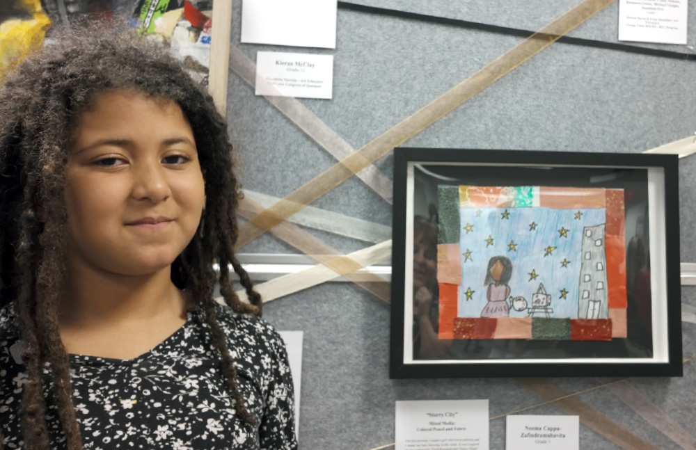 Neema Cappa-Zafindramahavita smiling next to her framed artwork