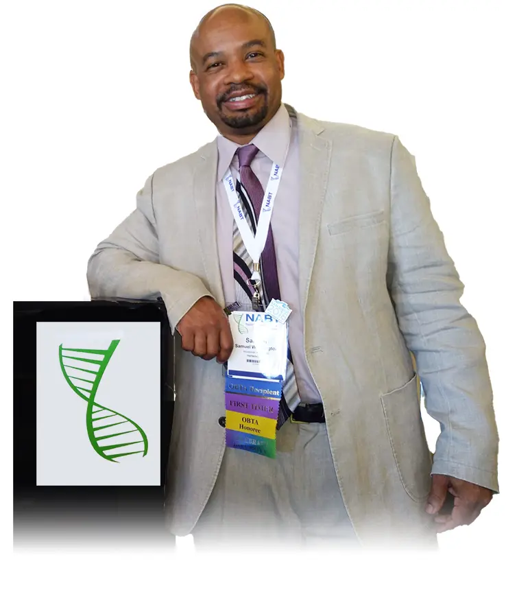 Sam Washington Jr. smiles dressed in a suit and tie, wearing an ID badge, leans on a stand displaying a green DNA helix logo.