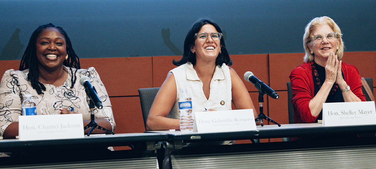 Three smiling female lawmakers or union leaders addressing an audience at a speaking event