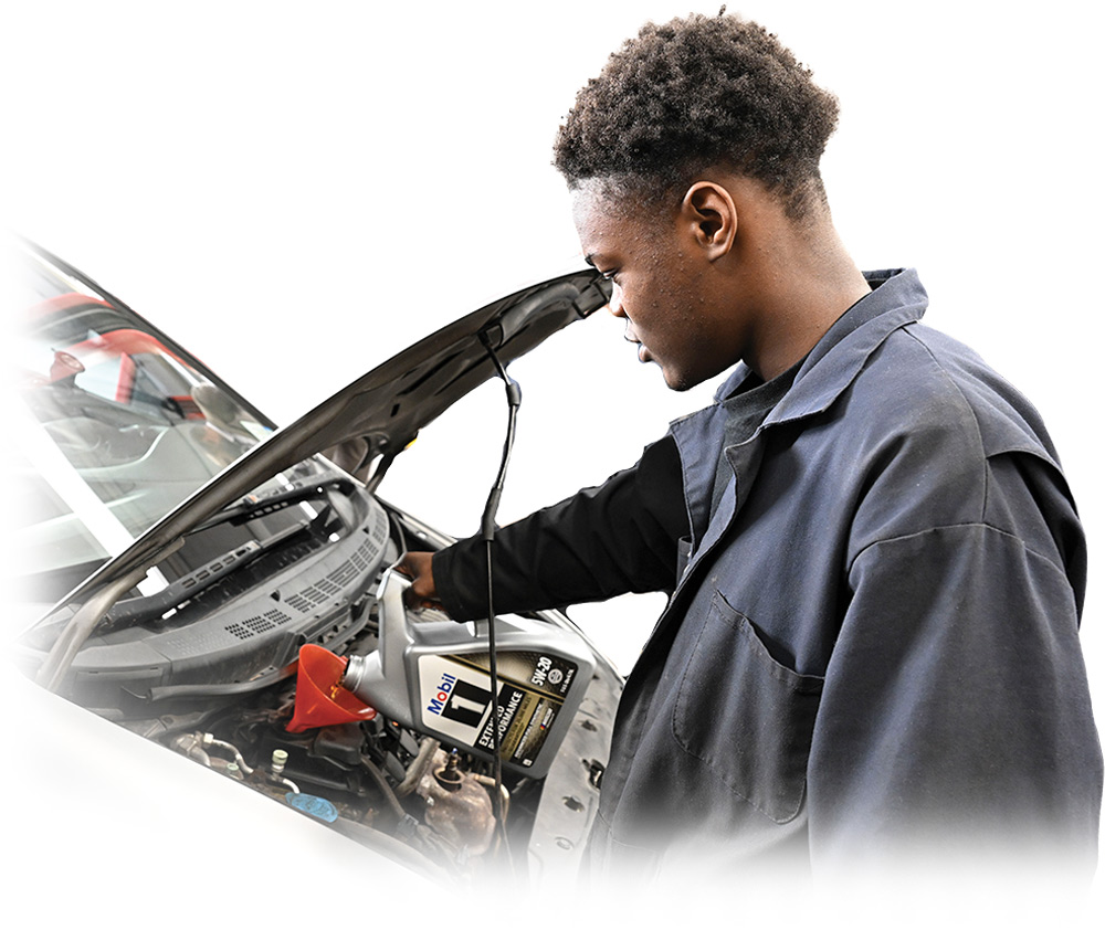 Person in a work uniform pouring oil into a car engine using a red funnel.