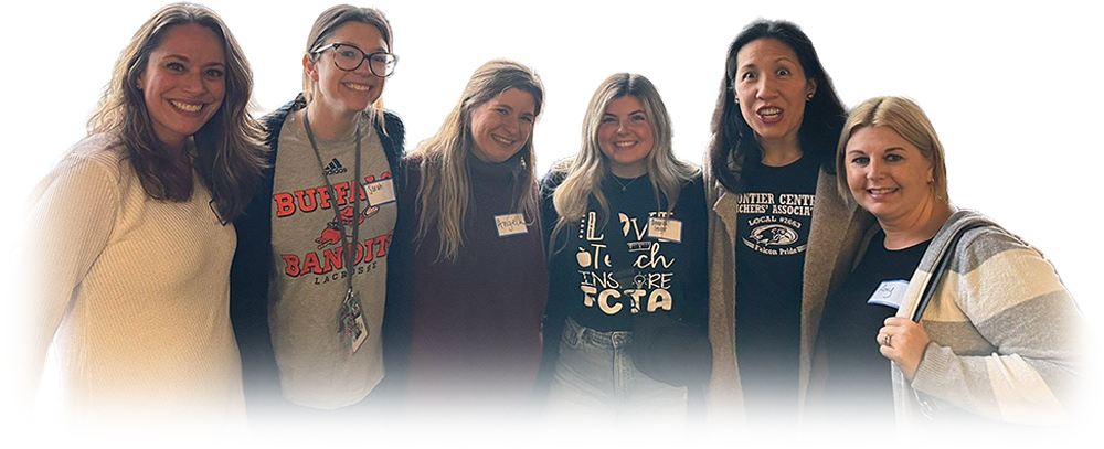A group of six smiling women standing together indoors with name tags.
