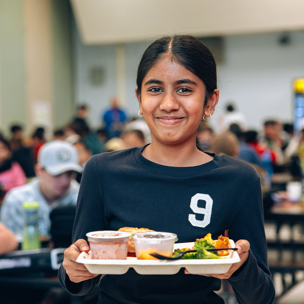 A smiling student at Iroquois Middle School holds a free universal meal tray in the school cafeteria.