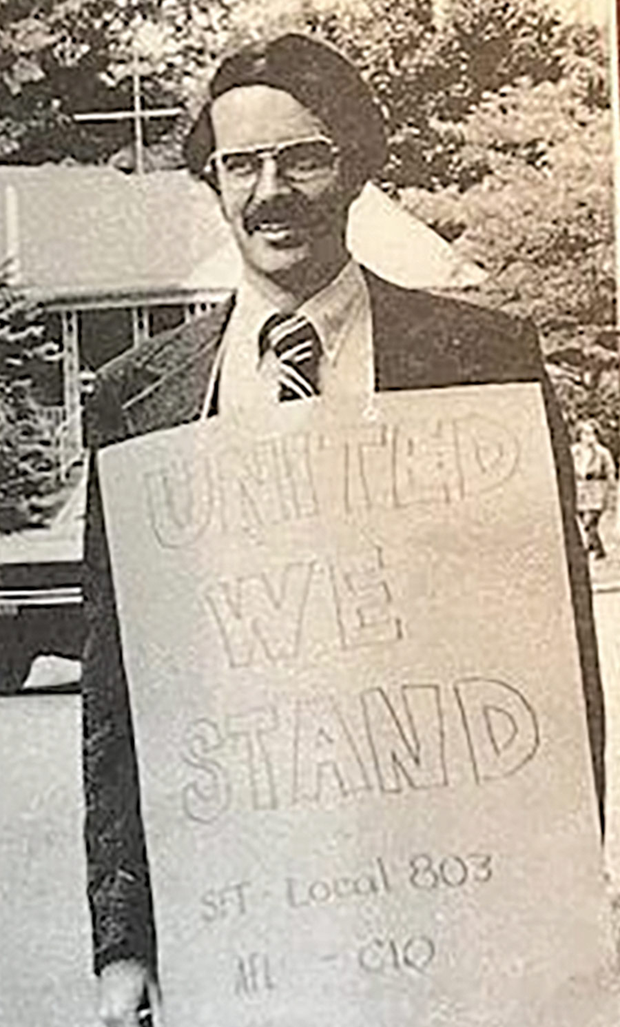 Black and white photo of a Schenectady teacher during the 1975 strike, wearing a picket sign that reads: UNITED WE STAND, SFT - Local 803, AFL-CIO.