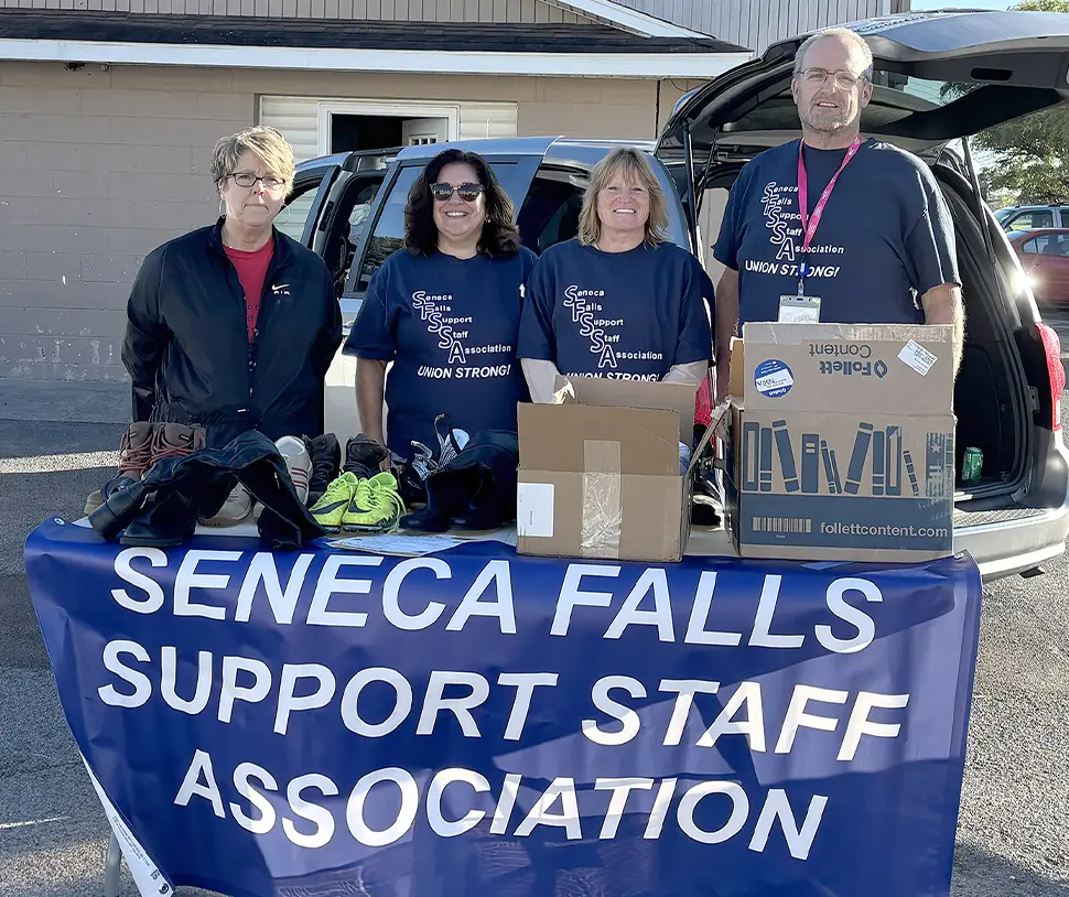 Marnie Impastato, Michelle Carmen, Chris Greer, and James Marley posing with boxes and a 'Seneca Falls Support Staff Association' banner