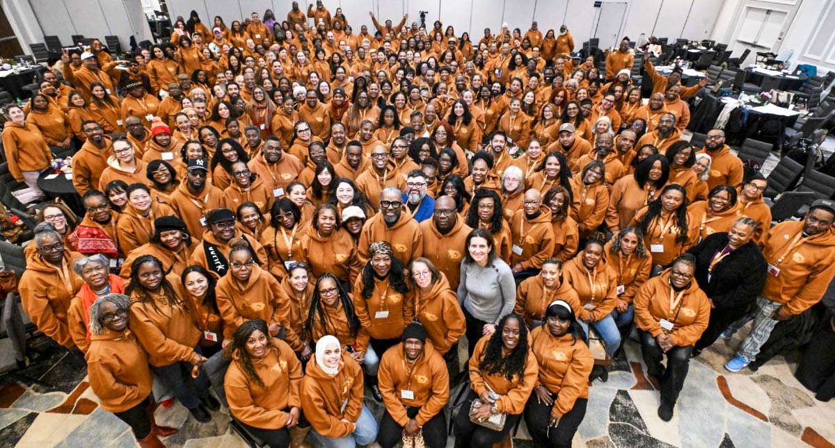 A large group of people wearing matching orange hoodies posing together in a conference hall.