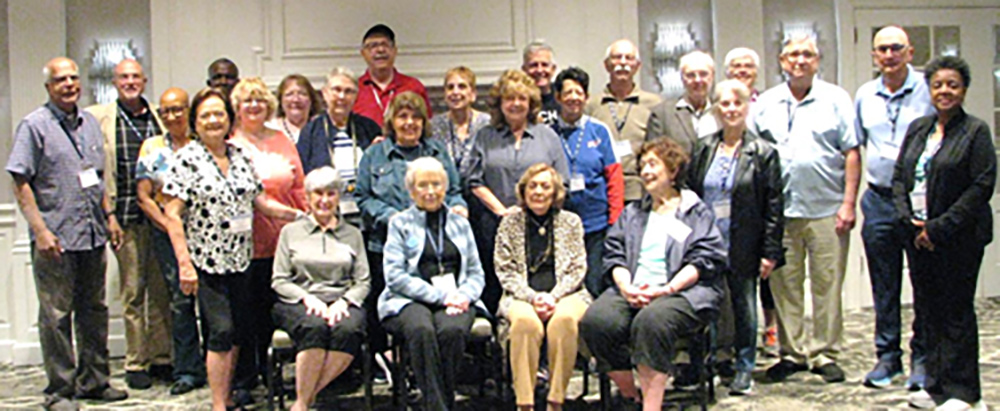 A large group of smiling retirees posing together for a group photo in a formal event hall.