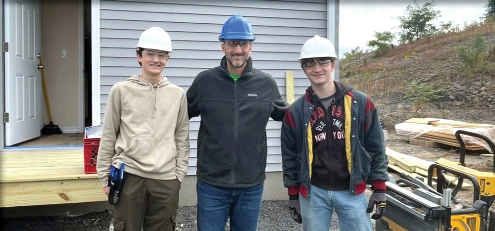 Three men wearing hard hats pose for a picture in front of a building.
