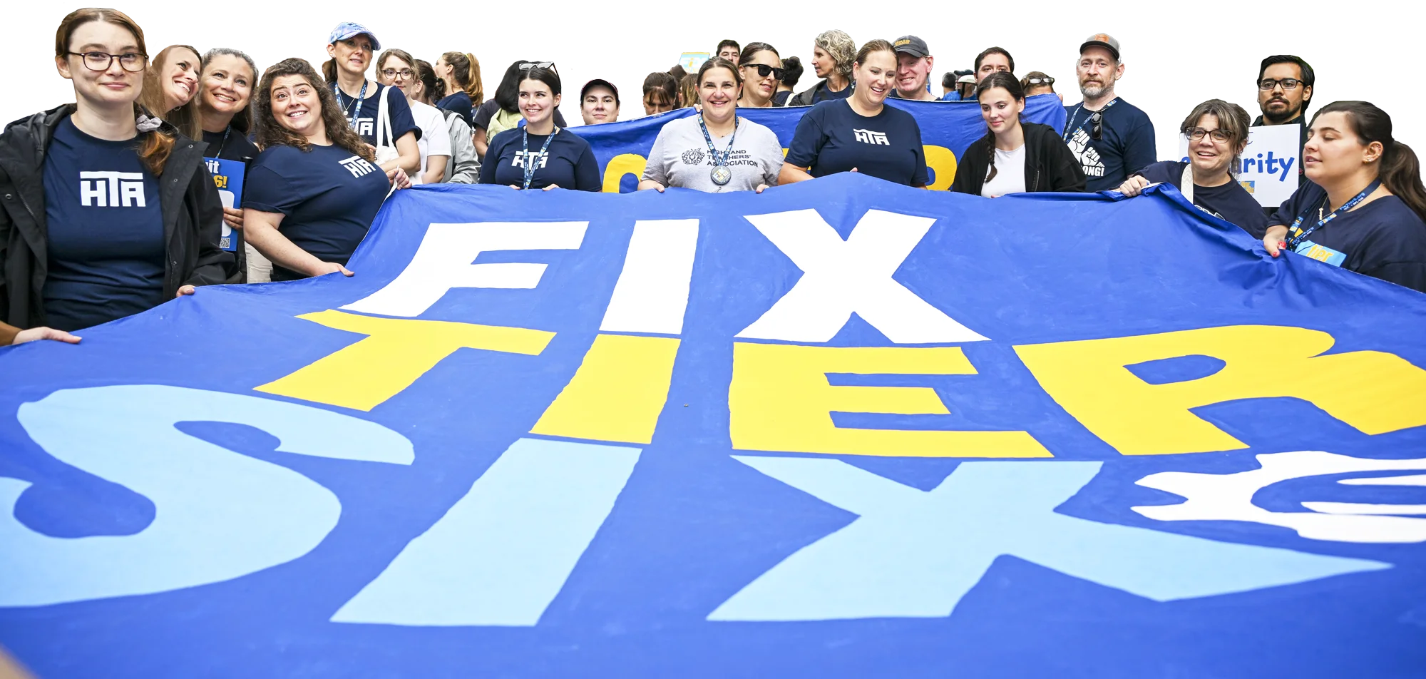 A large group of people, many wearing navy blue HTA shirts, stand together holding a wide blue banner that reads "FIX TIER SIX" in large white and yellow block letters.