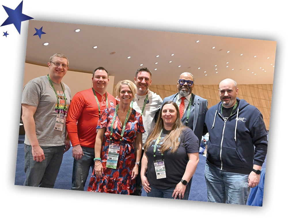 A group of seven smiling NYSUT conference attendees posing together for a photo in a convention hall.