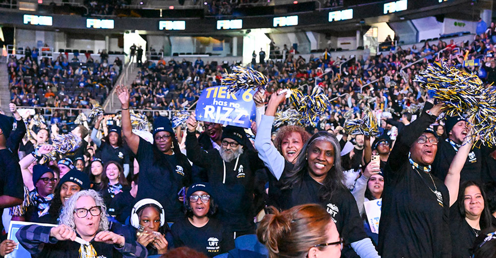 A large crowd of people in a stadium cheer and wave blue and yellow pom-poms. One person holds a sign that reads “TIER 6 has no RIZZ.” Digital displays in the background show the “FIX” logo.