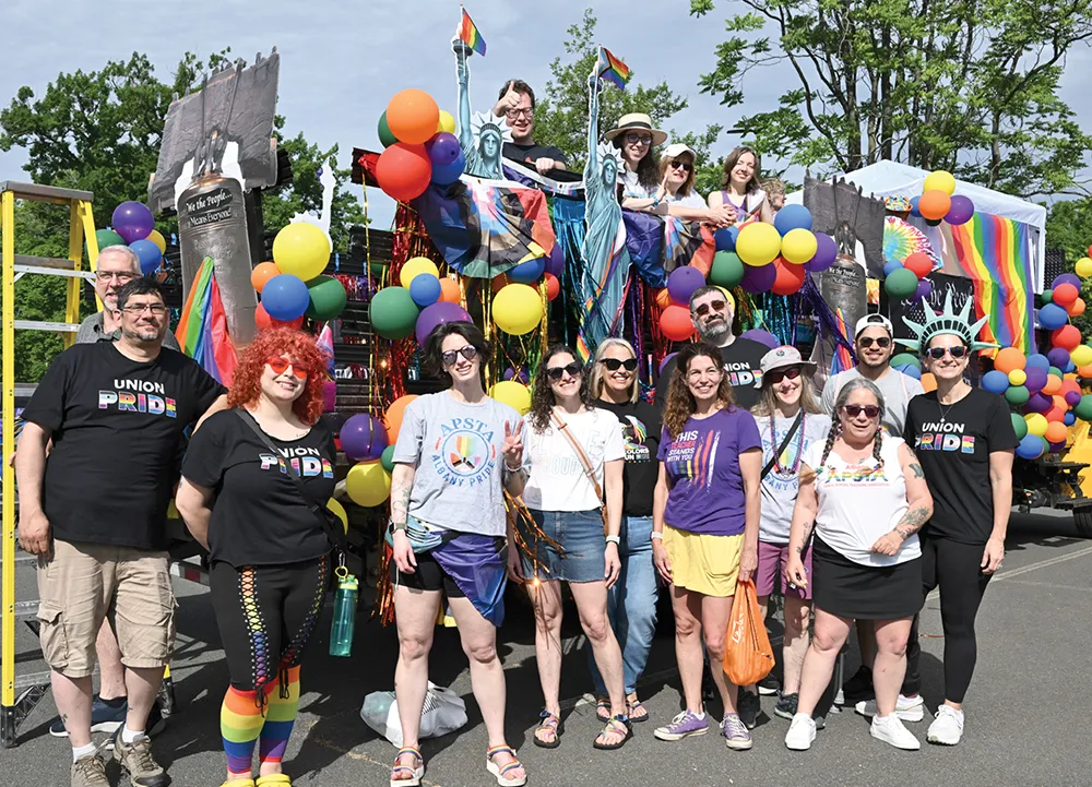 Group poses in front of a colorful Pride parade float decorated with rainbow flags, balloons, and "Union Pride" shirts.