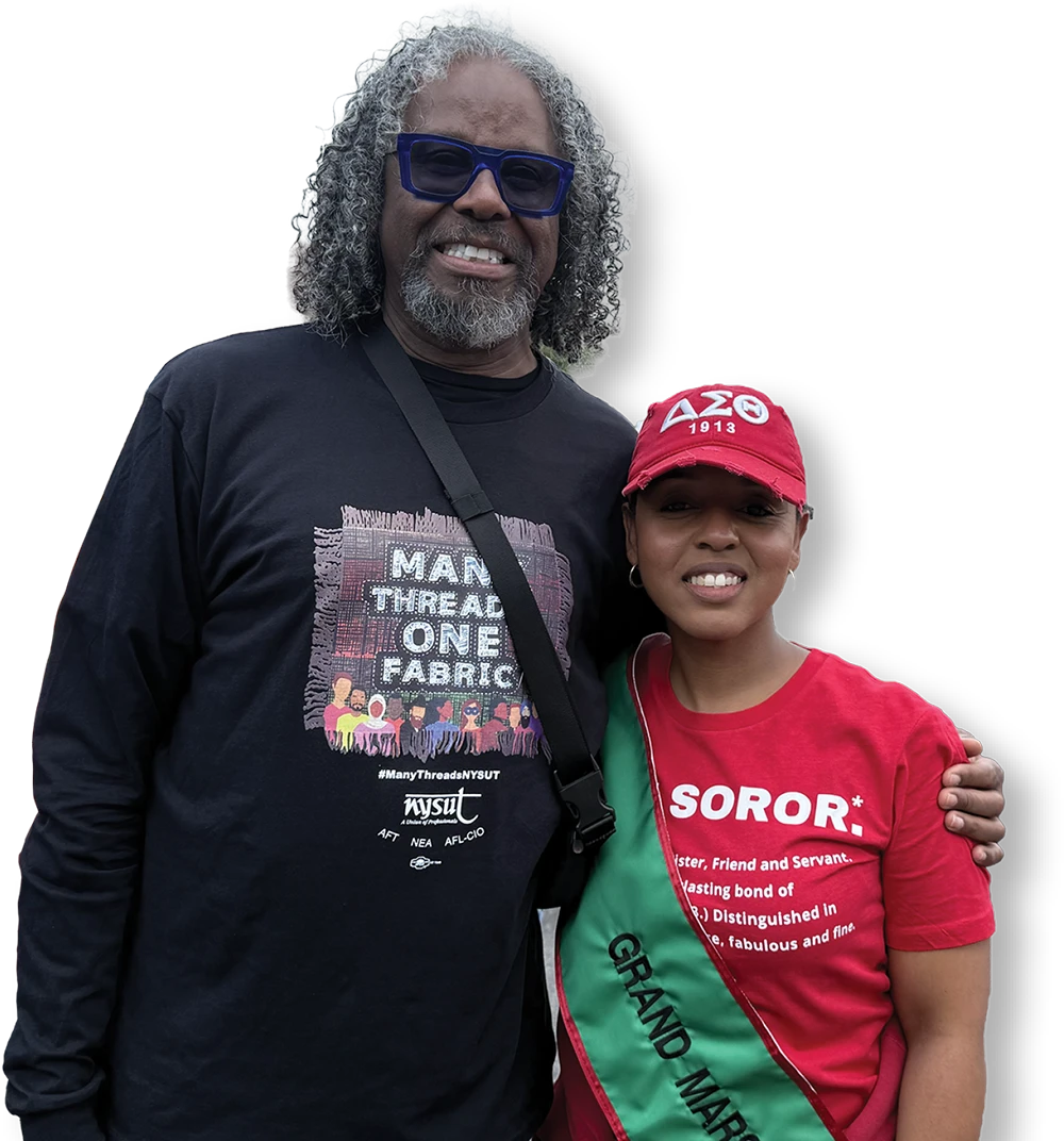 A man in a "Many Threads One Fabric" shirt stands with a woman in a red "Soror" shirt and Grand Marshal sash.