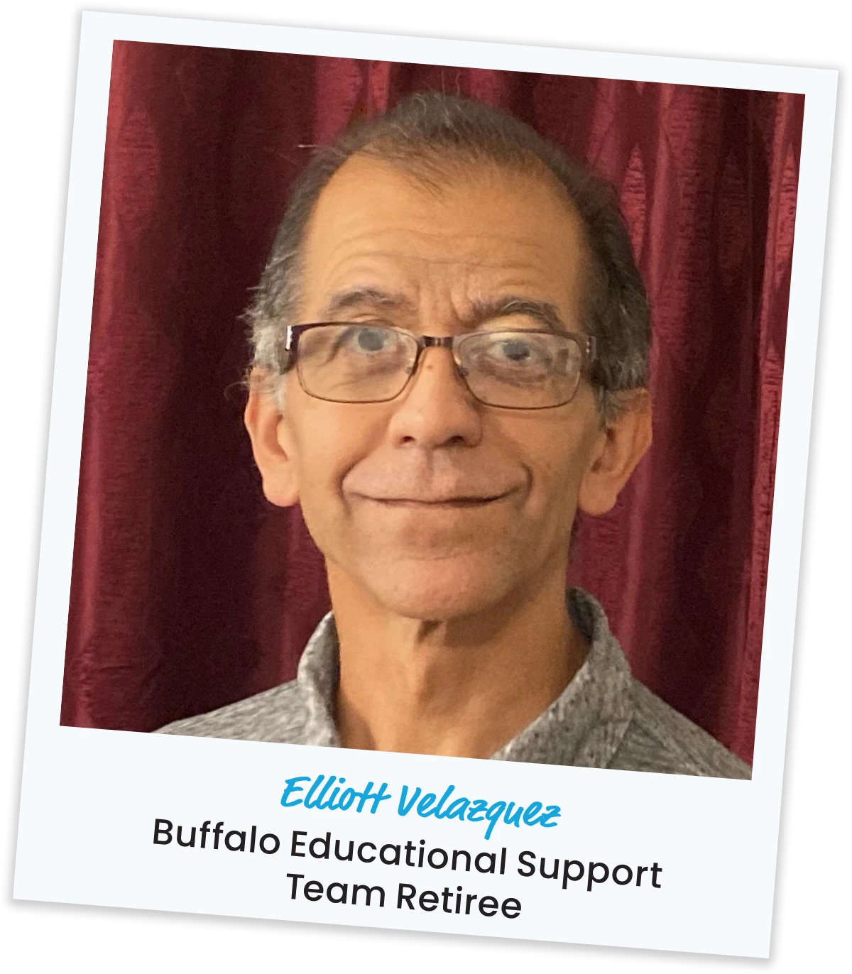 Close-up portrait of Elliott Velazquez from Buffalo Educational Support Team Retiree wearing glasses against dark red curtains.