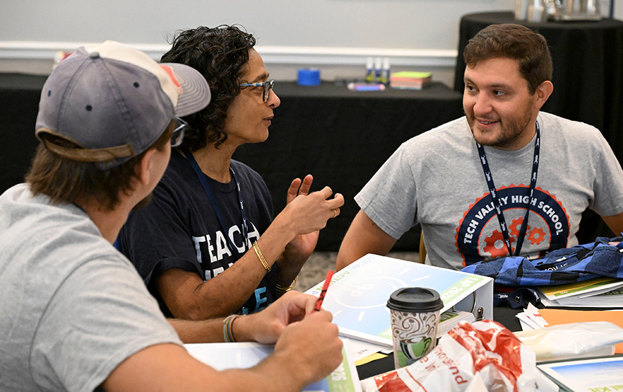 A group of three educators discussing materials at a workshop table.