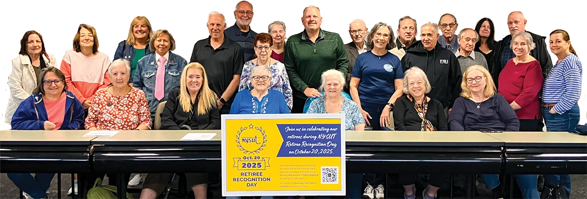 A large group of NYSUT retirees posing behind a table featuring a yellow and blue sign celebrating NYSUT Retiree Recognition Day.