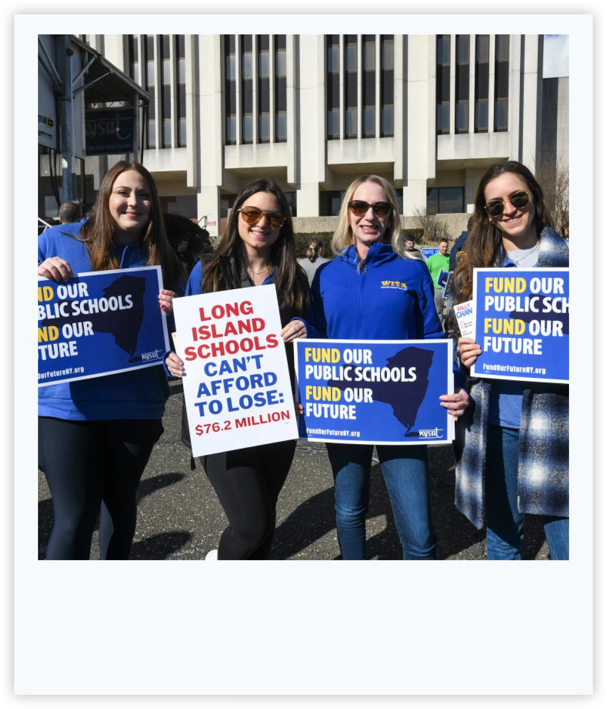 Four women holding signs advocating for public school funding, including one reading "Long Island Schools Can't Afford to Lose."