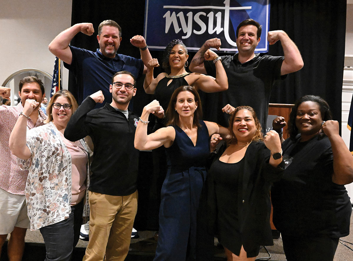 Group of people posing together and flexing their muscles in front of a NYSUT banner.