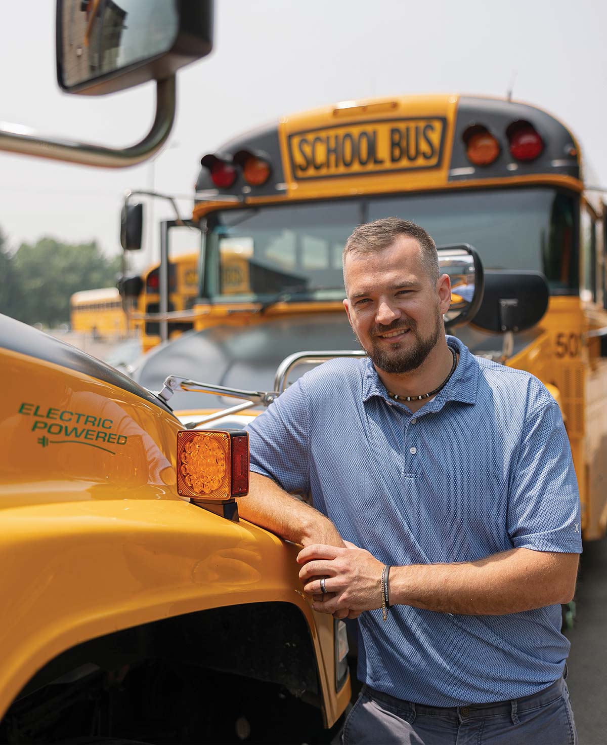 Man smiling as he leans against a yellow electric-powered school bus.