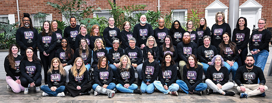A large group of people wearing matching black "SJA" long-sleeve shirts posing for a photo.